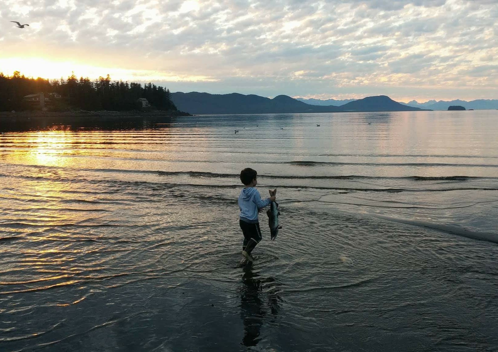 A child holds a salmon in front of a coastal inlet in Southeast Alaska.