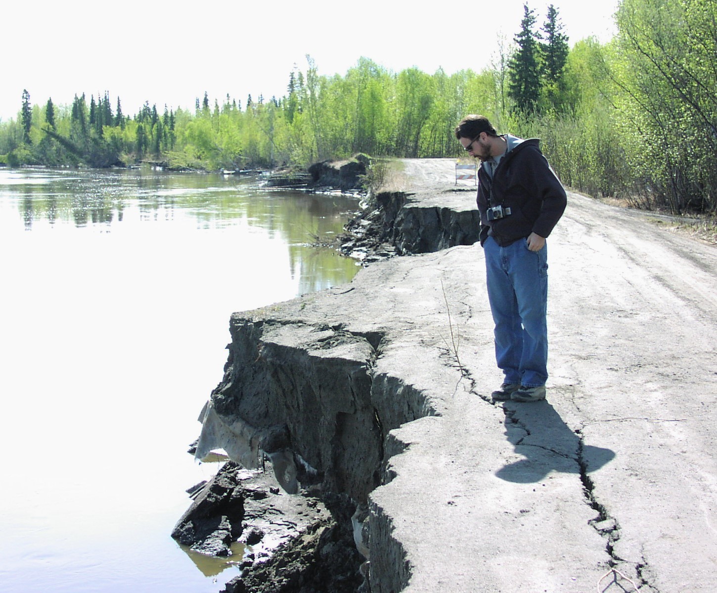 A man looks over the eroding riverbank in McGrath.