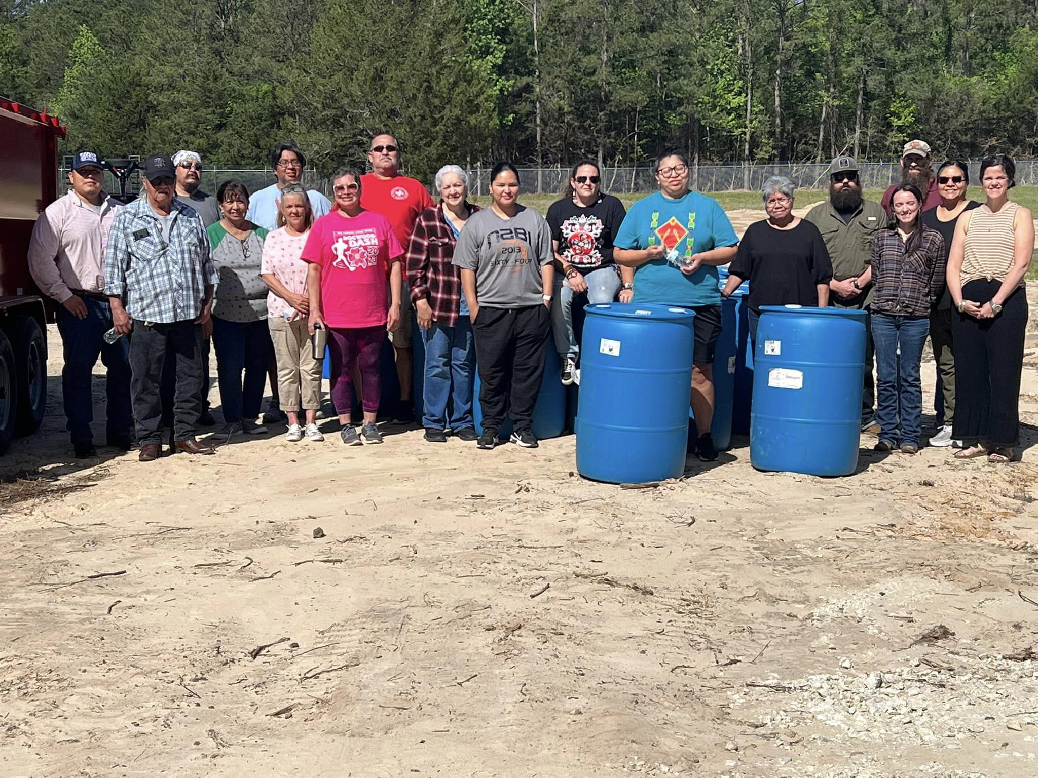 Tribal members standing with two blue rainwater harvesting barrels.
