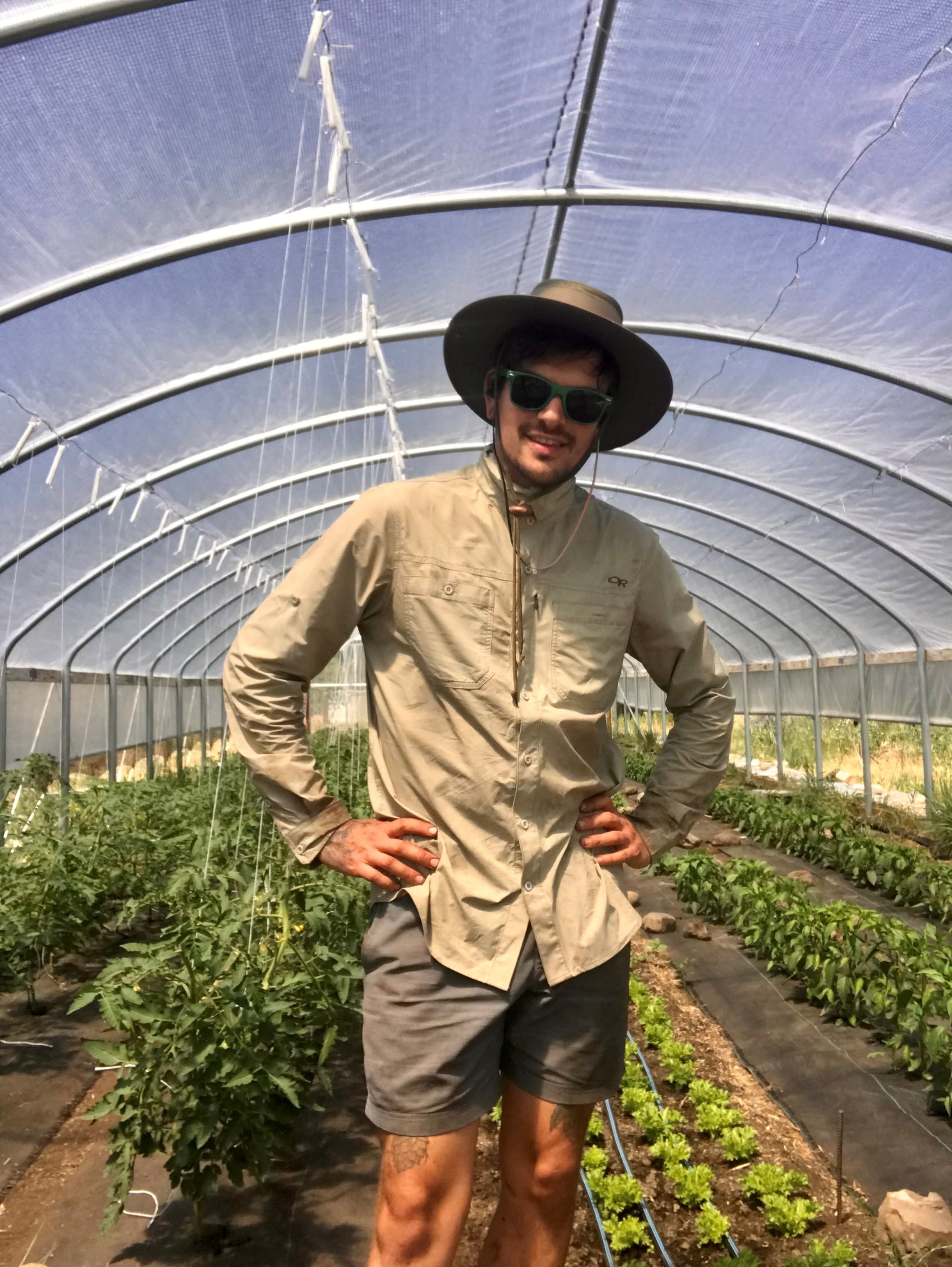 Farmer Brandon stands beneath one of his high tunnels, smiling.