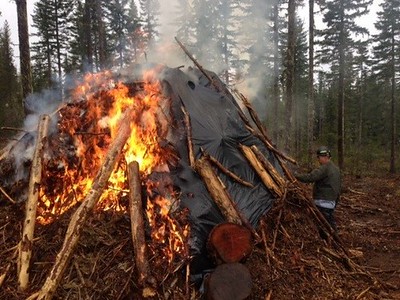 A pile of forest fuels being burned with a firefighter monitoring the progress.