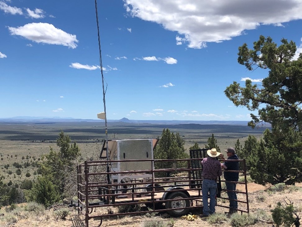 Two ranchers work to put up a tall GPS tower on rangelands.