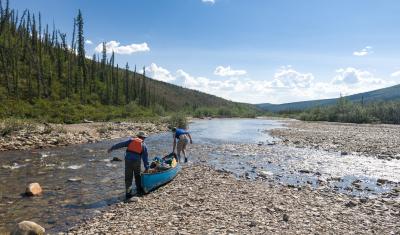 Two paddlers carry a canoe over a mostly-dry riverbed. 