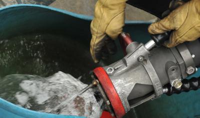 A person wearing tan leather gloves holds a large hose that is filling a turquoise bucket with a mixture of biofuel.