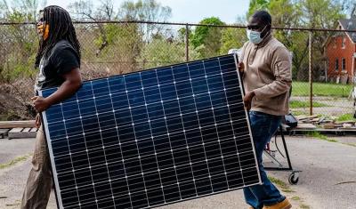 Two men carry a solar panel.