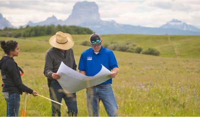 People looking at a map on a rangeland landscape with trees and rugged hills in the background.