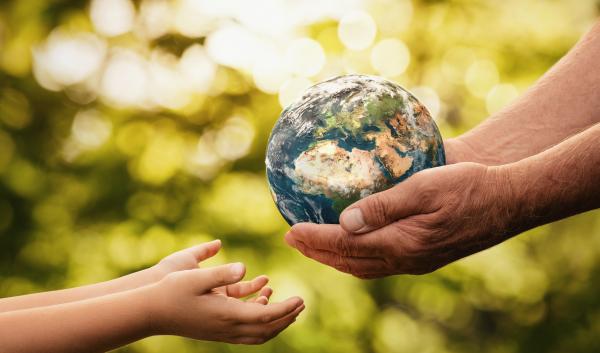 An adult hands over a miniature Earth to a younger person.